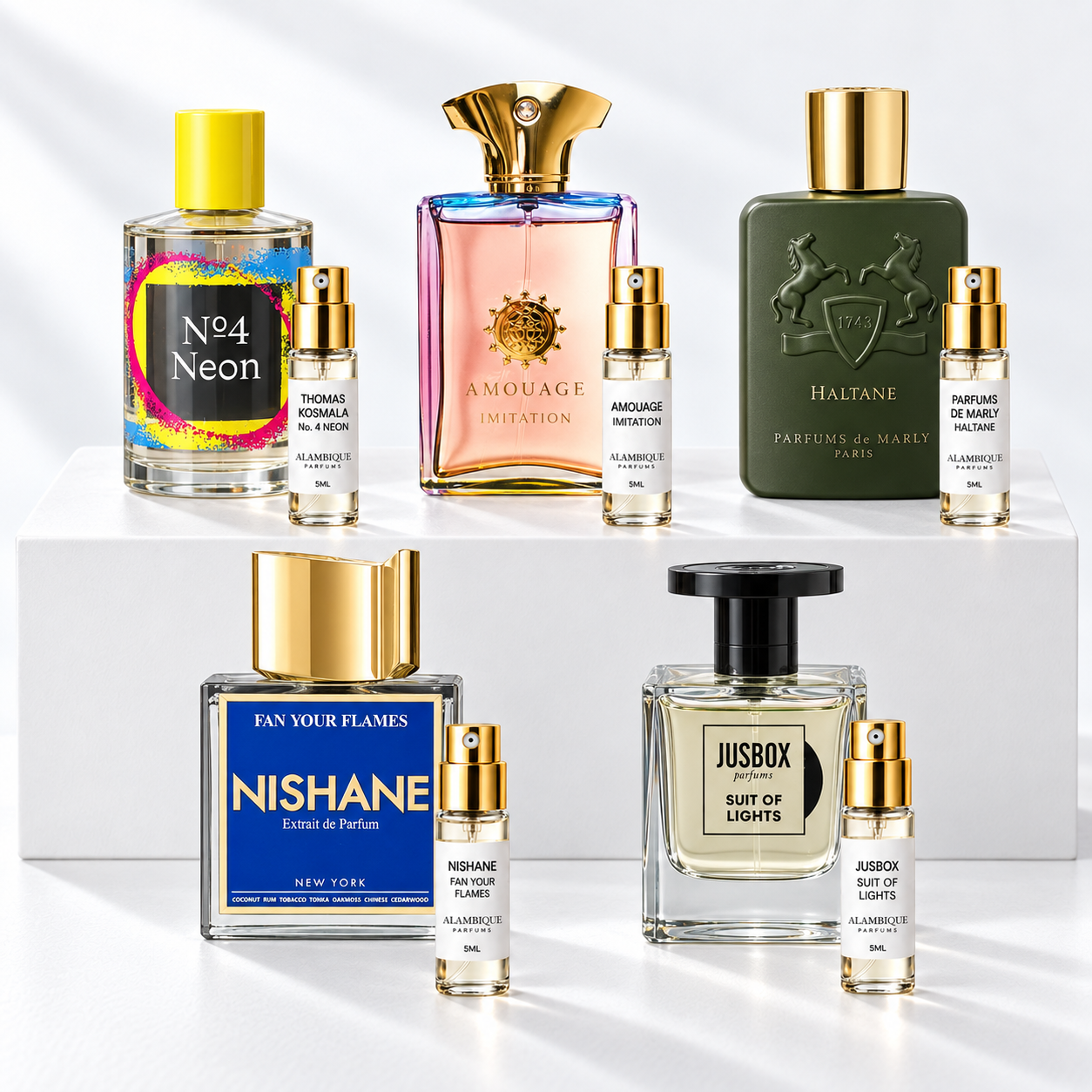 Discovery set Alambique: THOMAS KOSMALA No. 4 NEON, AMOUAGE IMITATION, PARFUMS DE MARLY HALTANE, NISHANE FAN YOUR FLAMES, JUSBOX SUIT OF LIGHTS. Decants con etiquetas blancas y atomizadores dorados junto a las botellas de referencia.